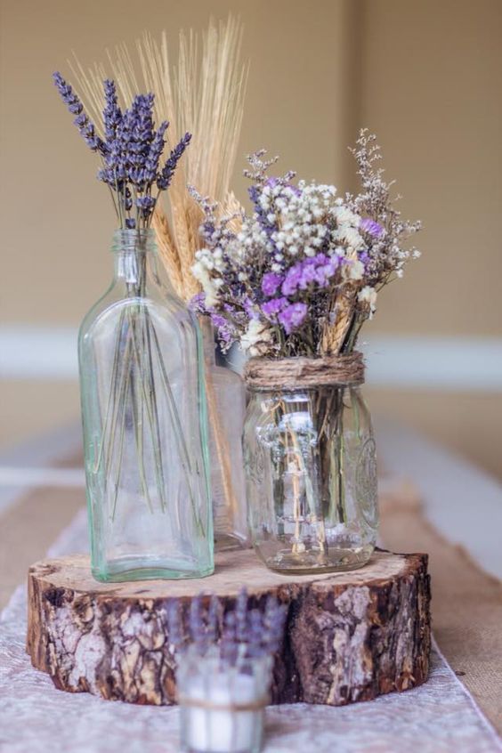 Mélange de fleurs séchées lavande et épis de blé dans des vases en verre portés par un rondin de bois